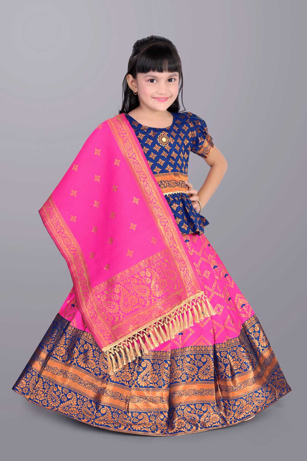 Young girl wearing a traditional pink and blue outfit with a matching shawl on a gray background