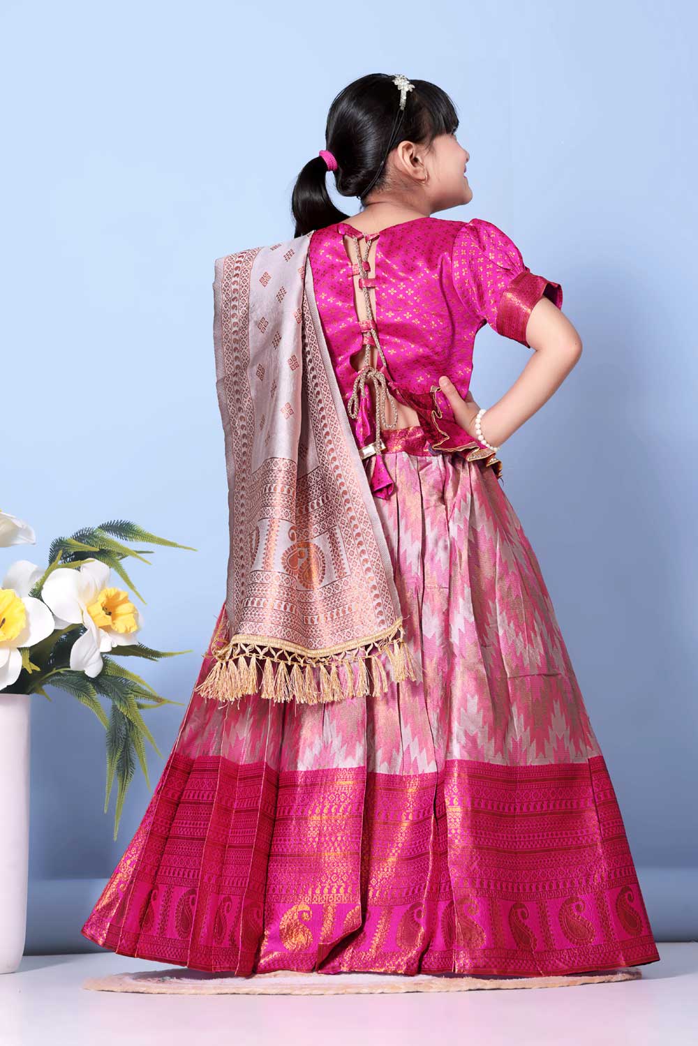 Young girl wearing a pink traditional outfit with a beige dupatta against a light blue background